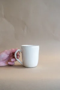 Hand houdt een handgemaakte Peachy Cream mok van Iris Floor Ceramics vast, met roze- en oranje tinten.