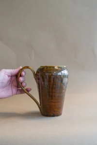 Handgemaakte Tigers Eye karaf met een hand die het handvat vasthoudt, glanzend bruin glazuur met gouden accenten.